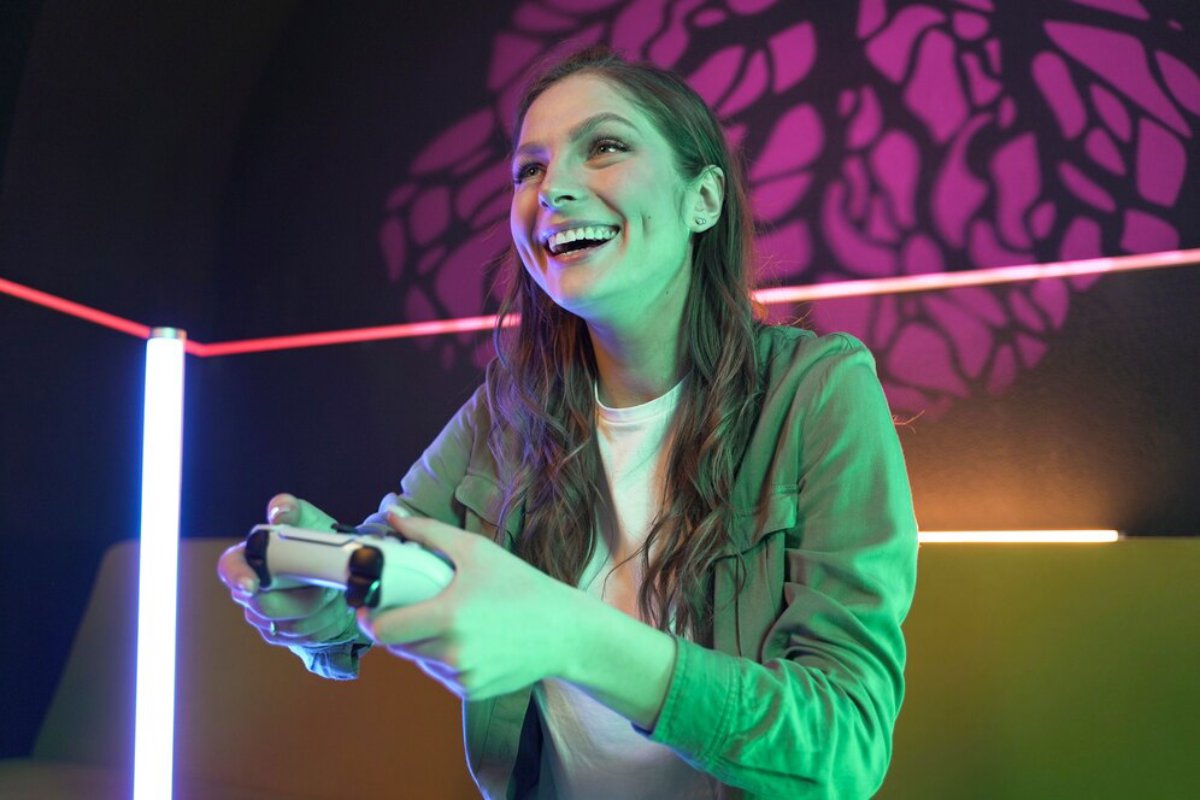 A person focused on gaming, holding a controller in a softly lit room with colorful LED lighting and textured shadows on the wall.