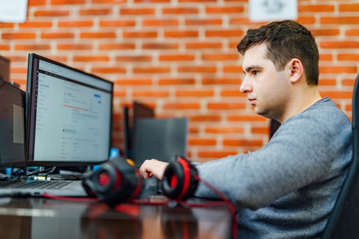 A person seated at a desk, focused on dual monitors displaying spreadsheets, with gaming headphones resting nearby.