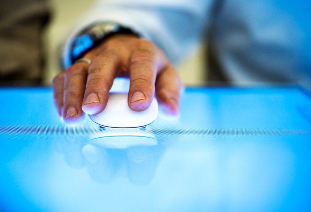 A close-up of a hand using a white computer mouse on a digital screen with a blue glow, indicating interaction with technology.