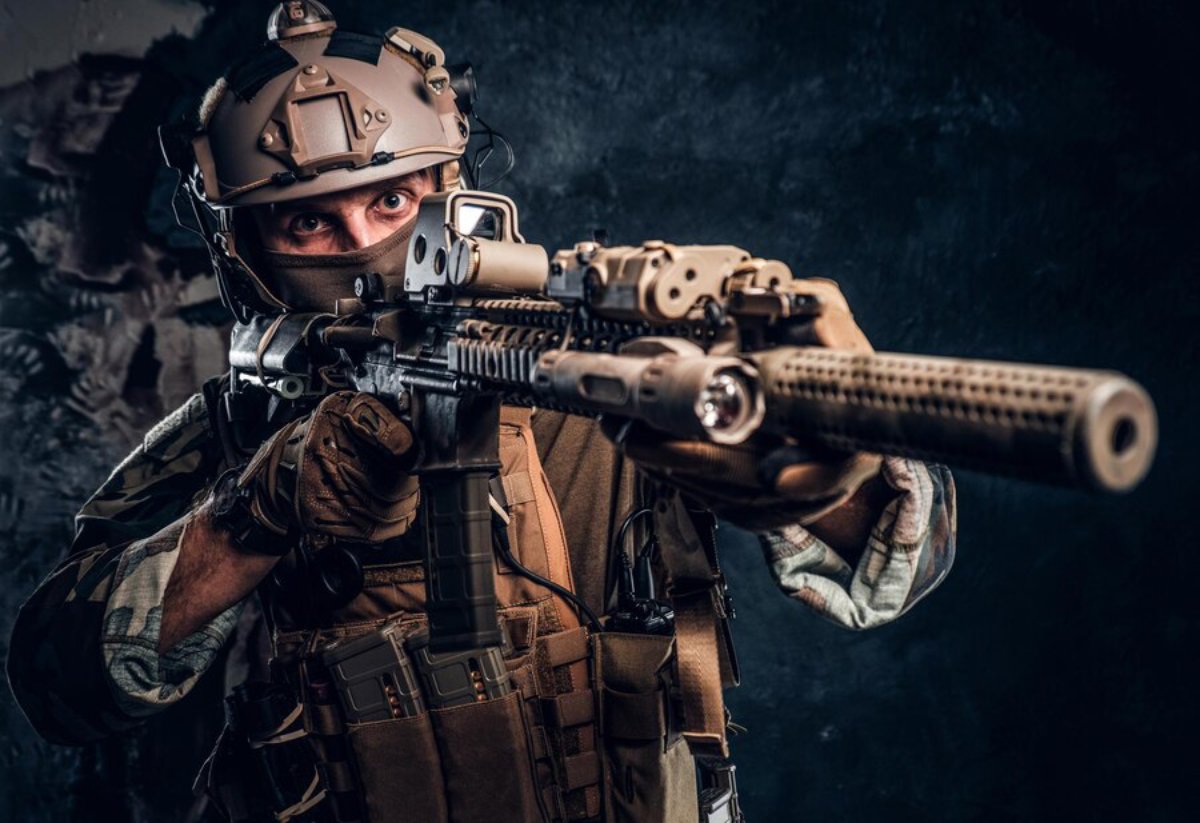 An armed soldier in tactical gear aims a rifle, illuminated against a dark, textured background, showcasing a serious demeanor.