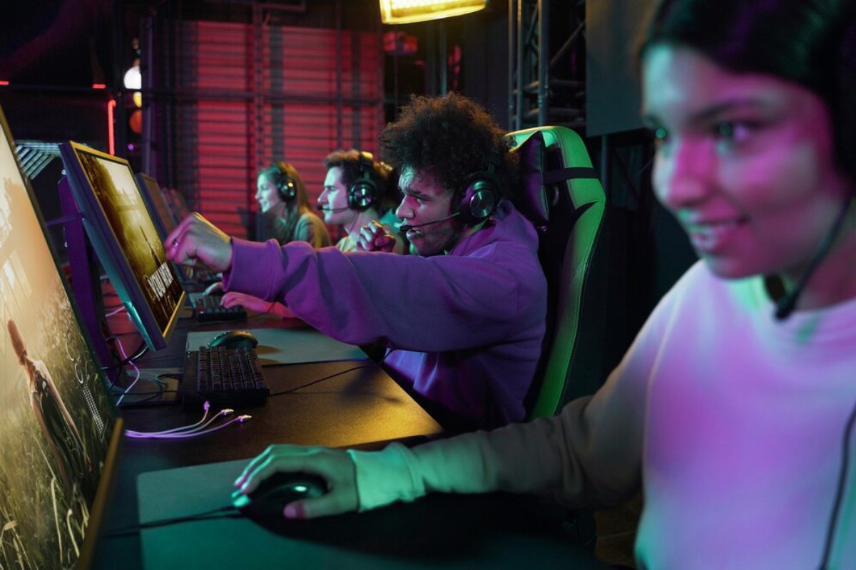A group of gamers engaged in intense play at their computers, wearing headsets and illuminated by colorful lights.