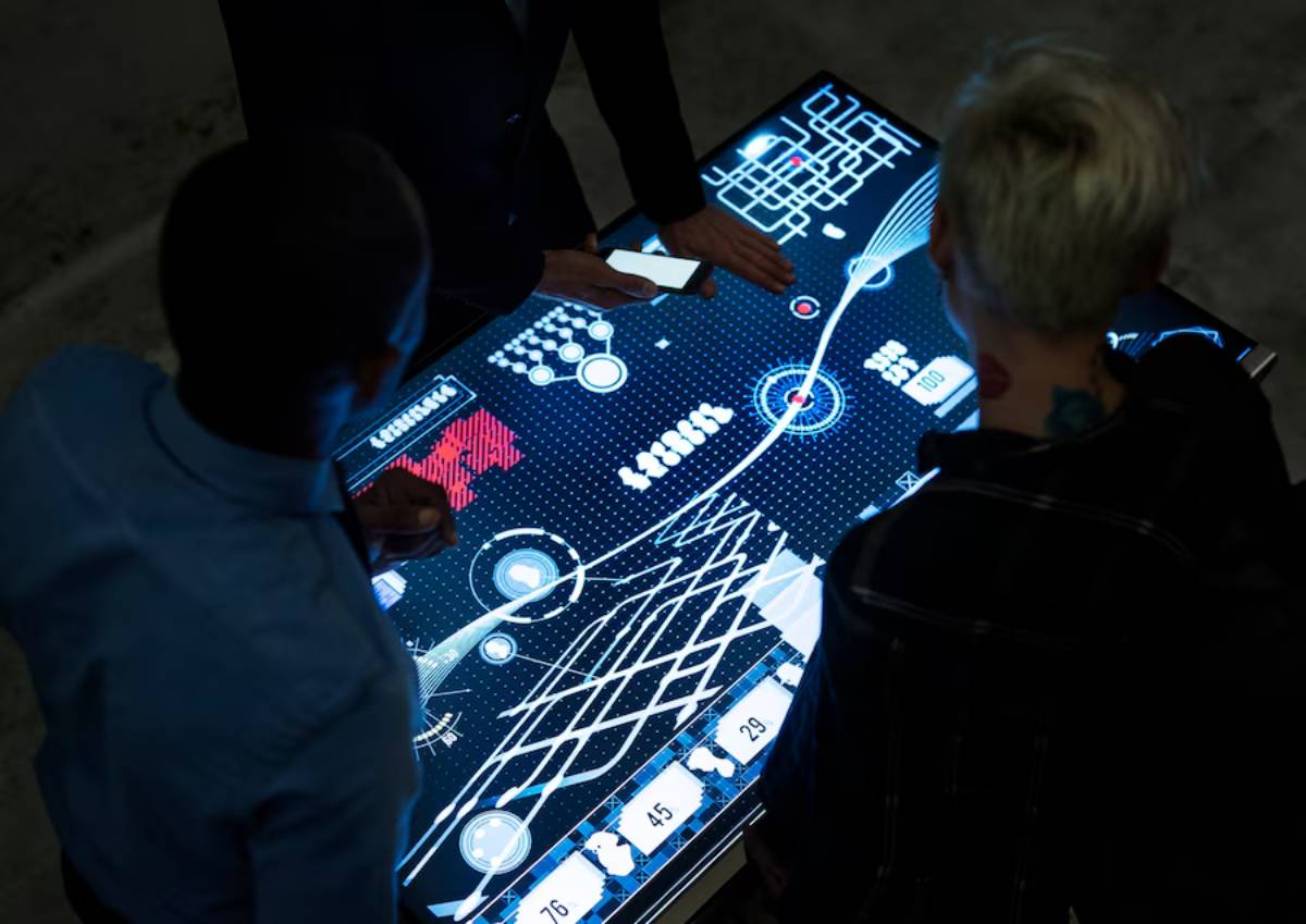 Two people interact with a large digital touchscreen displaying complex, colorful data visualizations and graphs.
