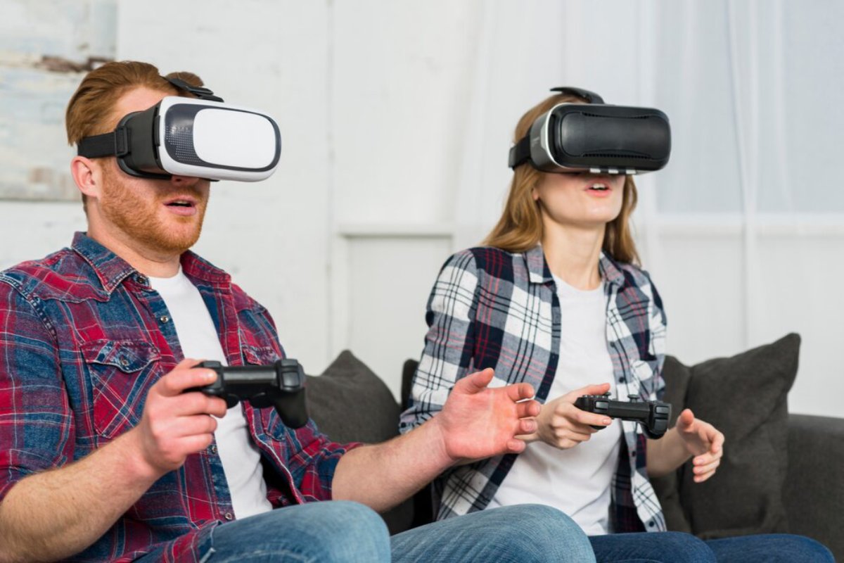 A man and woman are intensely engaged in virtual reality gaming on a sofa, both wearing VR headsets and holding controllers.