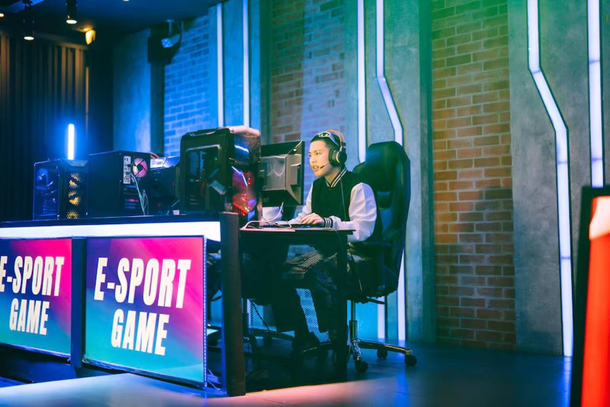 A gamer in a headset competes at an e-sports event, focused on dual monitors with colorful LED lights in a modern gaming setup.