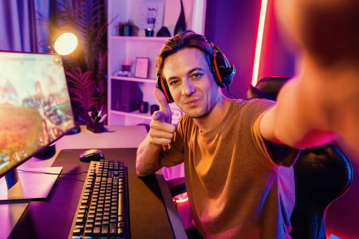 A group of gamers wearing headphones is focused on their computer screens in a dimly lit gaming lounge.