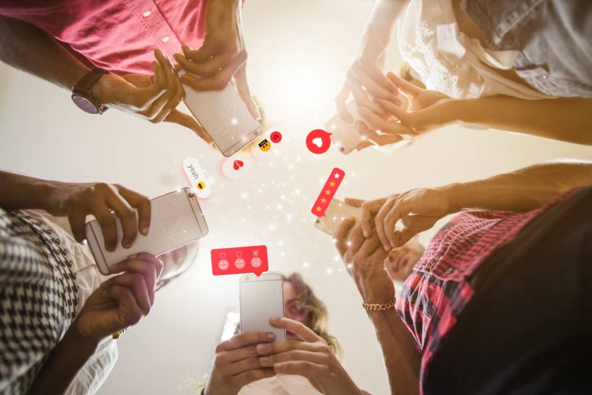 A group of people holds smartphones, surrounded by social media icons and emojis, showcasing digital engagement and connection.