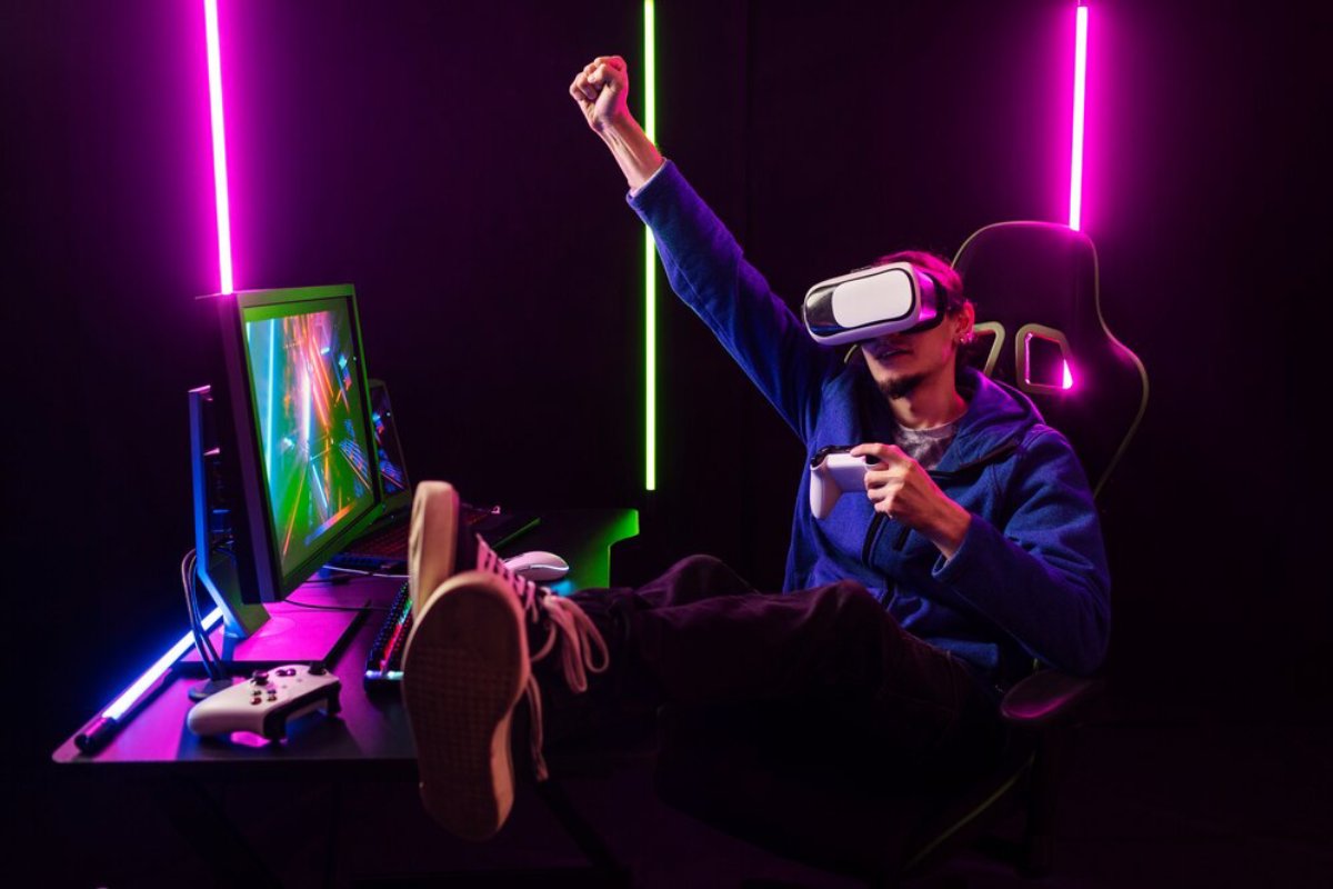 A person wearing a VR headset cheers with one arm raised while sitting in a gaming chair, surrounded by neon lights and gaming equipment.