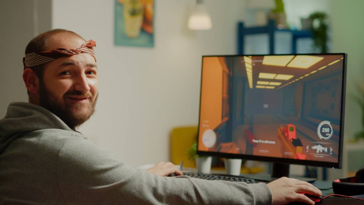 A gamer focuses intently on a vibrant computer screen displaying a shooting game in a cozy indoor setting.