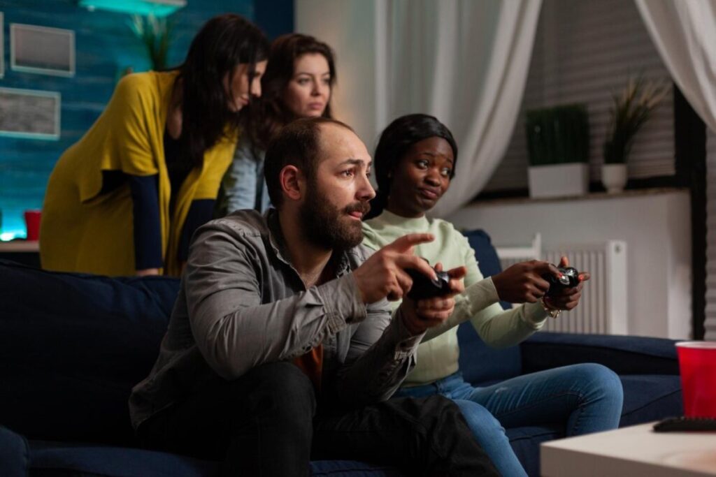 A group of friends engaged in a video game session, sitting on a dark blue couch in a cozy, well-lit living room.