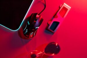 A gaming mouse, 3D glasses, and an hourglass on a surface lit with dramatic red and blue lighting.