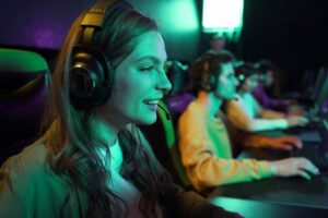 A group of gamers focused on their screens, wearing headsets, illuminated by colorful lights in an esports environment.