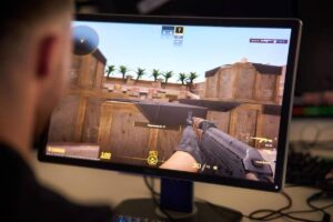 A close-up of a gamer playing a shooting game on a monitor, showing gameplay with an AK-47 and a tactical setting.