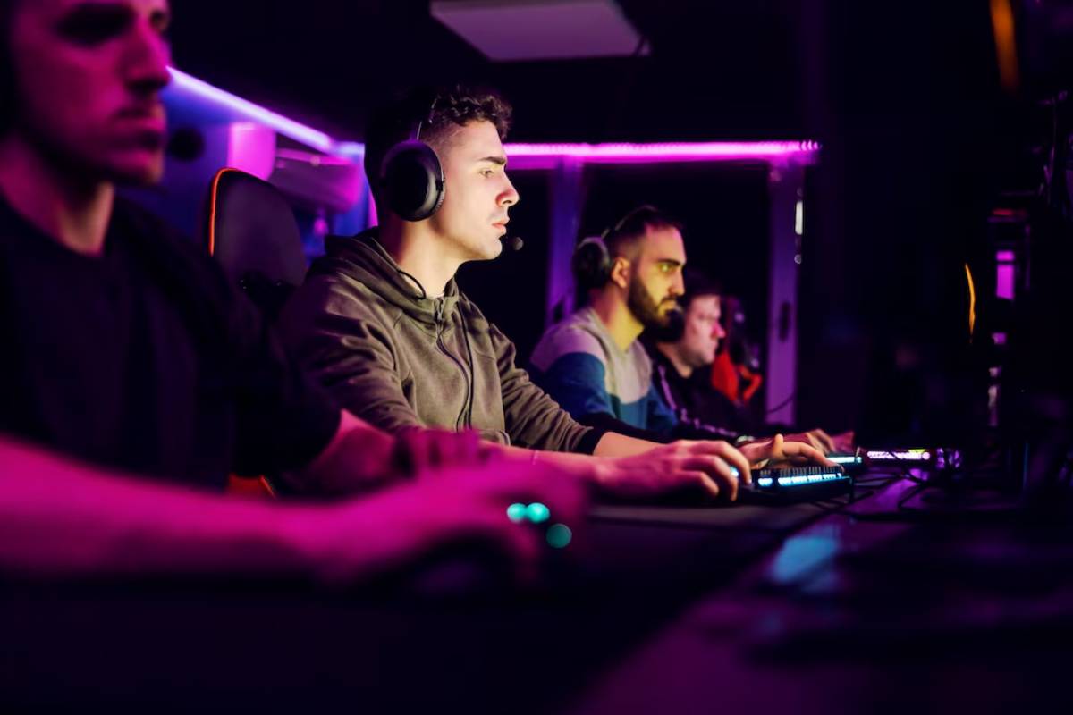 Group of gamers focused on their screens in a dimly lit room with colorful LED lighting, using headsets and gaming keyboards.